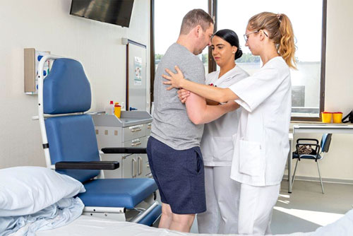 Two nursing students assisting a patient with standing up and walking.